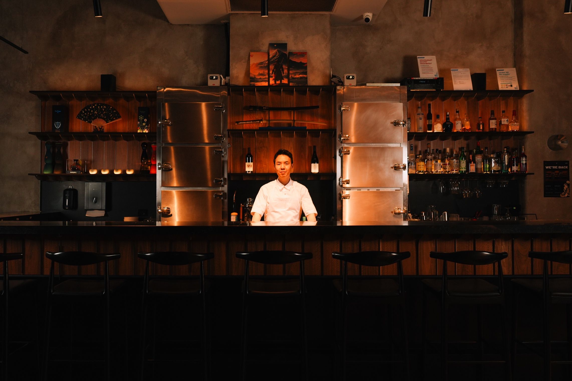 Chef standing behind the dimly lit bar counter at Ronin Omakase