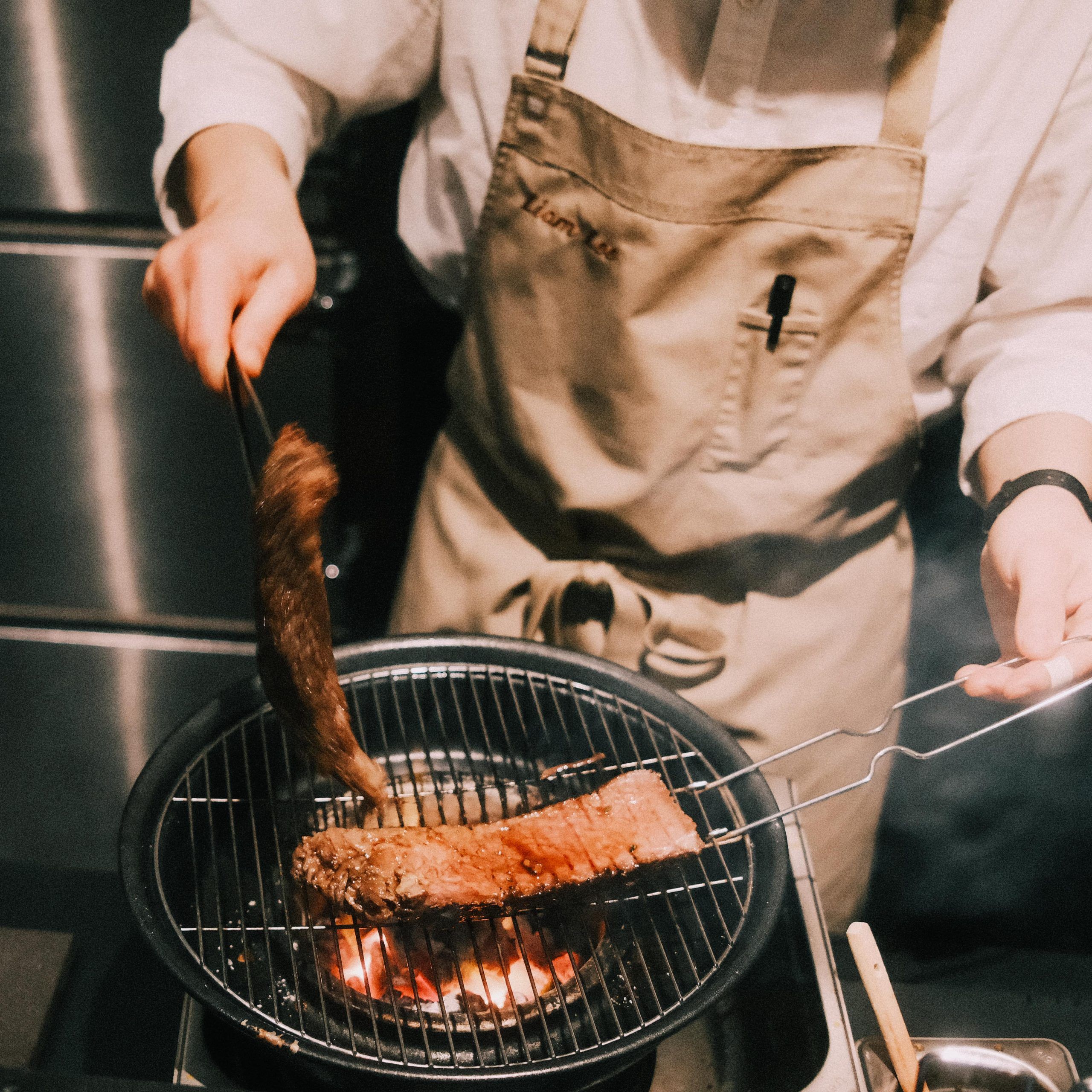 Chef lifting grilled beef off the charcoal at Ronin Omakase